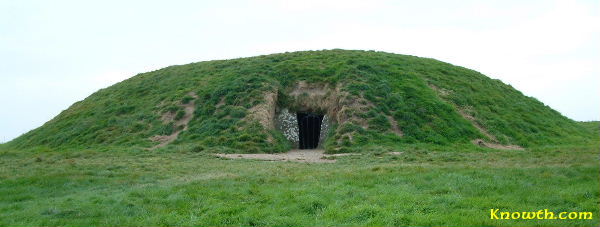 green hillside with a doorway craved into the side of it, its a dark and ominous hole that is prefectly shaped.